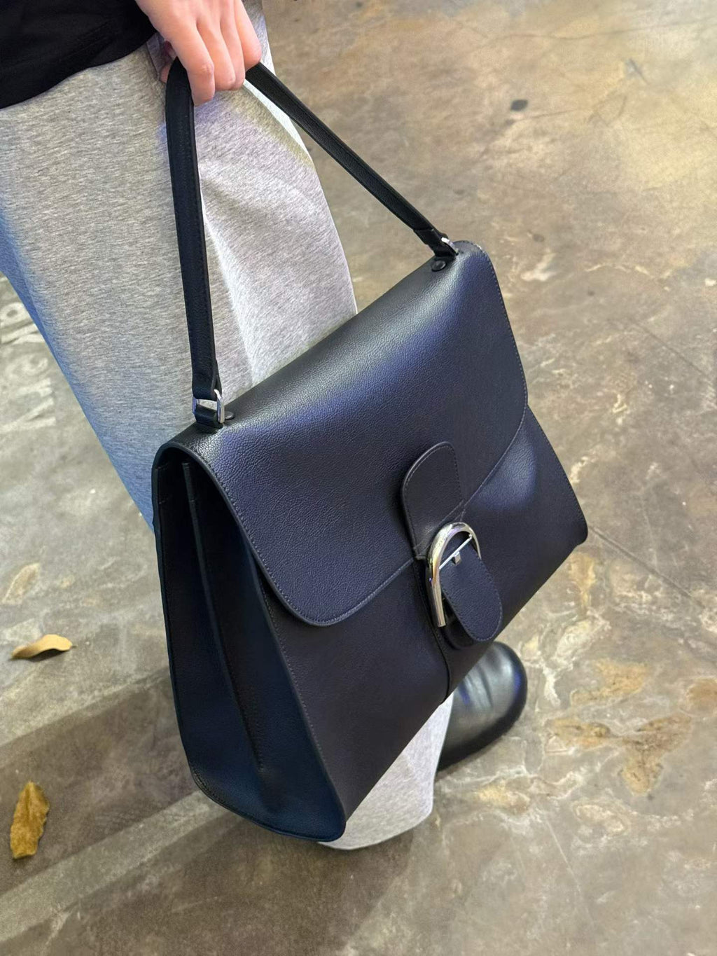 Black leather shoulder bag, designer style tote with structured flap, silver metal D-clasp closure, carry handle.