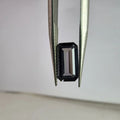 Gray emerald-cut spinel gemstone held between metal tweezers