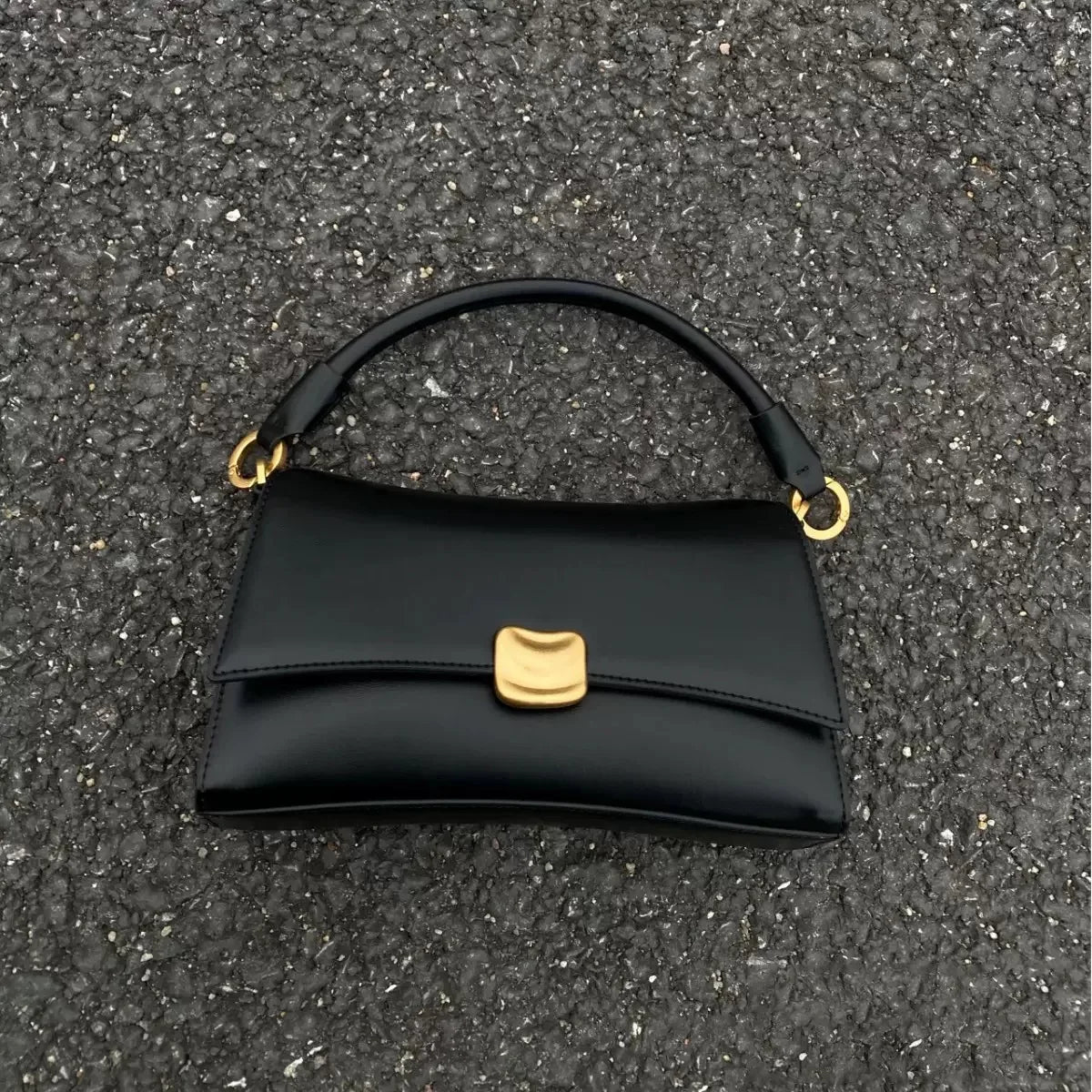 Black designer underarm handbag with gold magnetic clasp, structured square shape, and smooth leather-look finish.