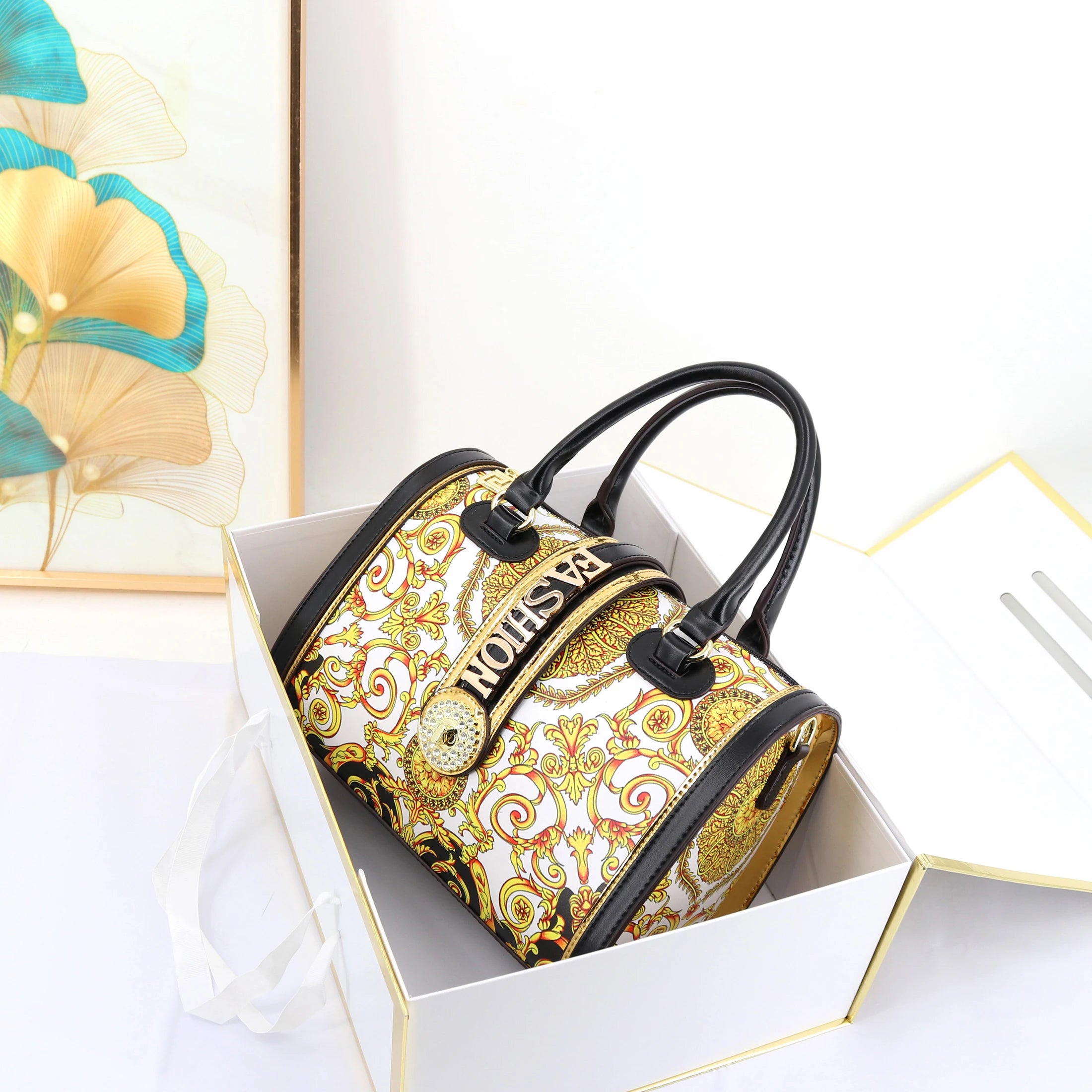 2026 designer trunk handbag with gold baroque print, black trim, and embellished "FASHION" center buckle. 29 cm.