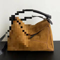 Tan suede designer handbag with structural paneling, black leather handle, and crossbody strap. Luxury 2025 style.