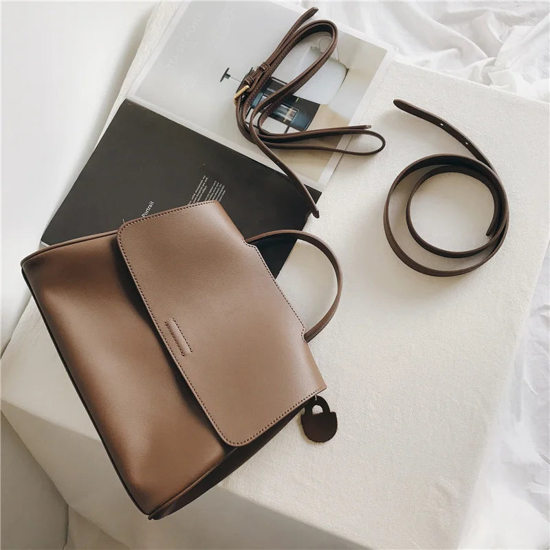 Minimalist brown leather designer handbag with a flap closure, top handle, and detachable crossbody strap.