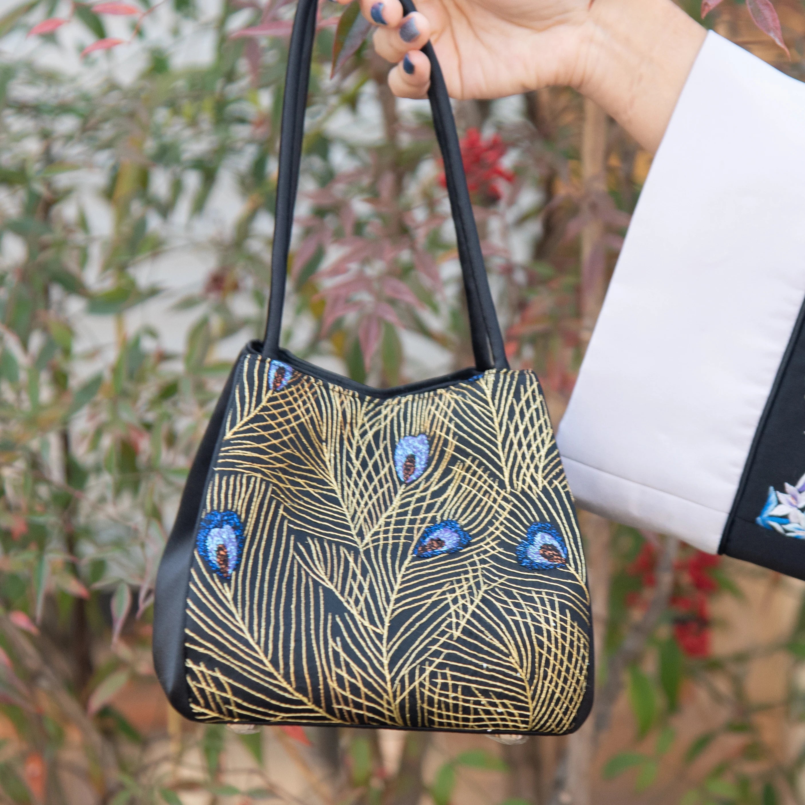 Black designer handbag with gold peacock feather Su embroidery and blue accents for daily use.