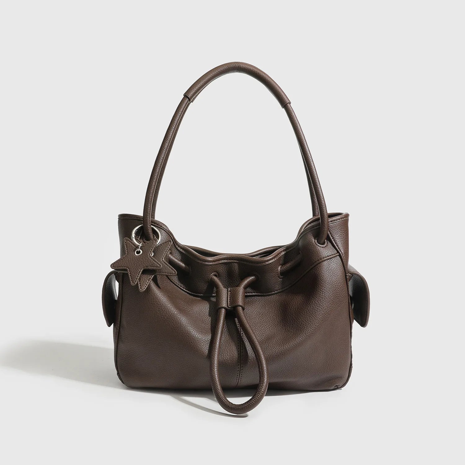 Dark brown pebbled leather shoulder bag with drawstring closure, two straps, and star charm for commuting.
