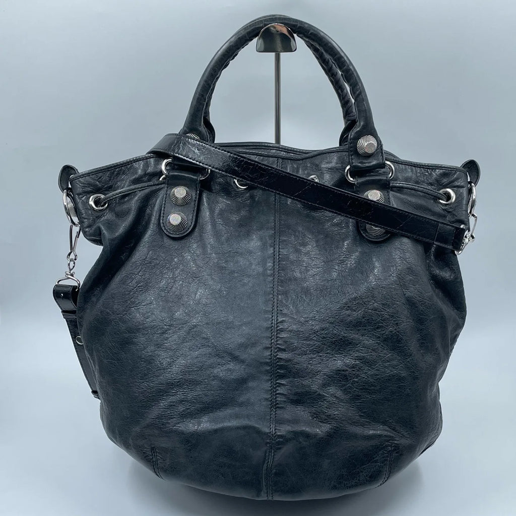 Pre-owned black leather designer bucket bag with silver metal studs, top handle, and adjustable shoulder strap.