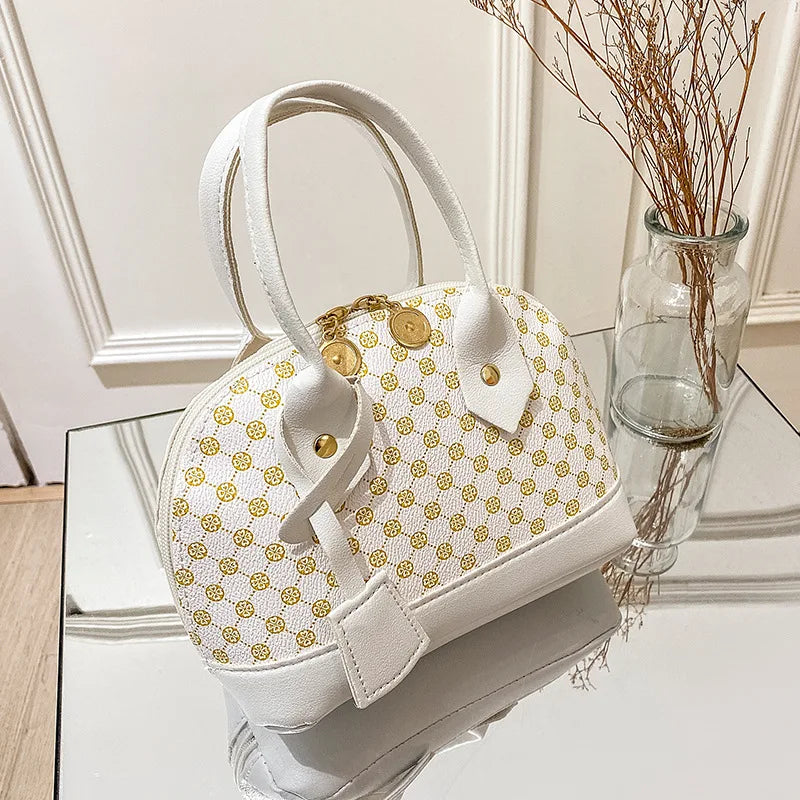 White designer shell handbag with gold geometric print, double handles, and metal zipper closure for daily use.