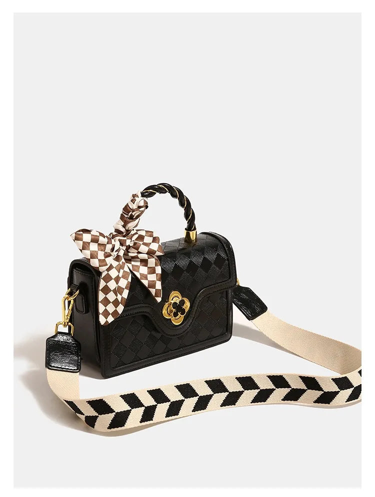Black quilted leather trunk bag with gold flower clasp, plaid silk scarf, and patterned crossbody guitar strap.