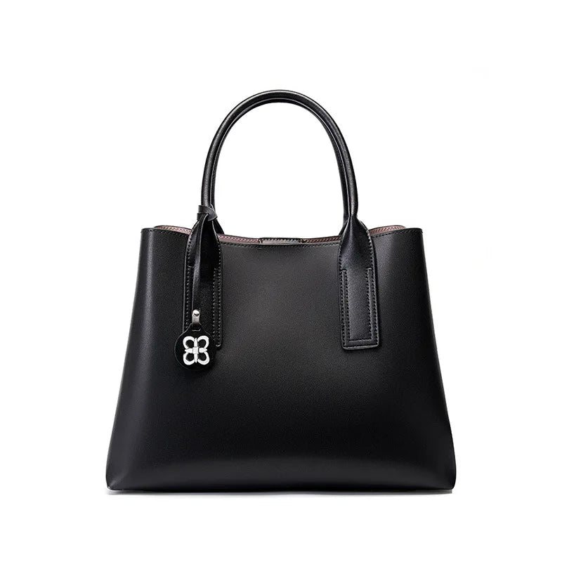 Elegant black genuine leather designer handbag with top handles, silver charm, and spacious structured silhouette.