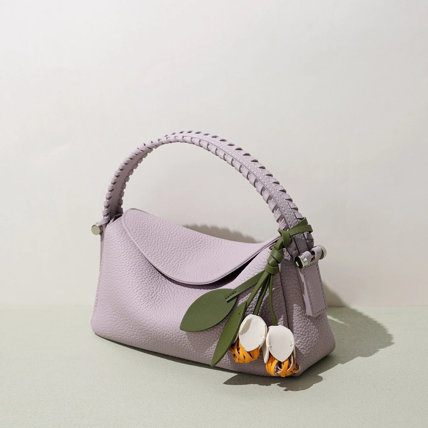 Lavender genuine leather crossbody bag with woven handle and whimsical flower charm in designer handbag style.