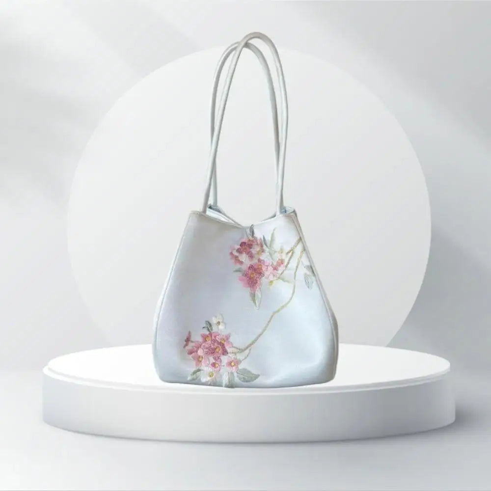 Luxury artisanal pale blue handbag with intricate pink Su embroidery floral design and slim shoulder straps.