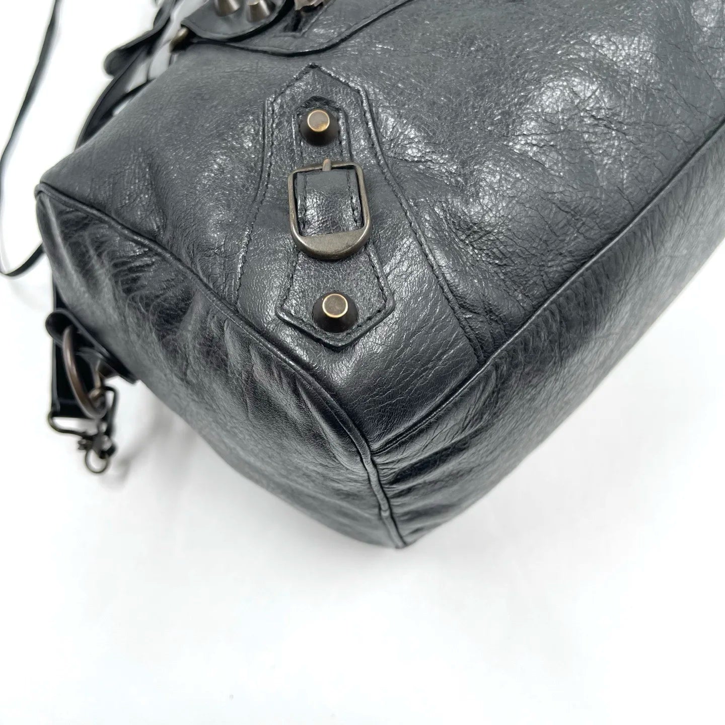 Black genuine leather designer handbag, pillow-shaped tote with vintage buckle hardware and distressed texture.