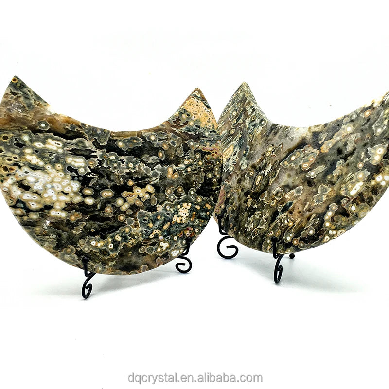 Two ocean jasper crescent moon crystals on black stands, dark green and cream dotted detail