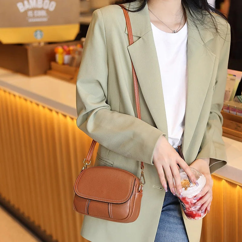 Brown genuine leather mini designer crossbody bag with white stitching detail, worn as a stylish shoulder bag.