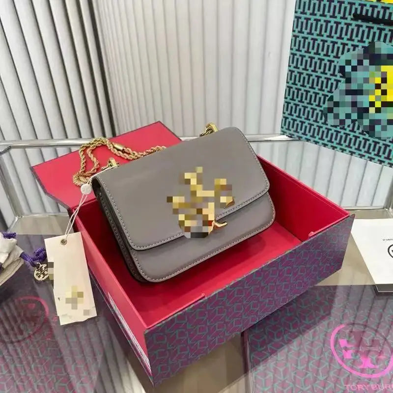 Grey leather trunk crossbody bag with gold metal logo, chain strap, and designer gift box.