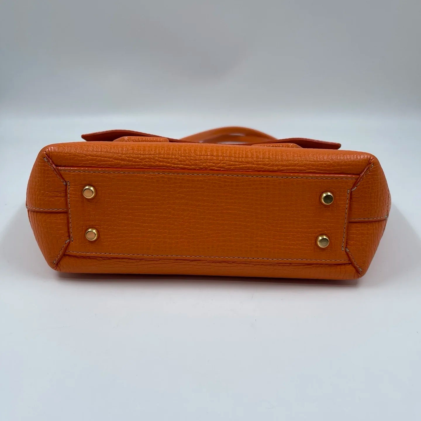 Orange genuine leather designer handbag bottom with protective gold-tone metal feet. Elegant luxury shoulder tote.