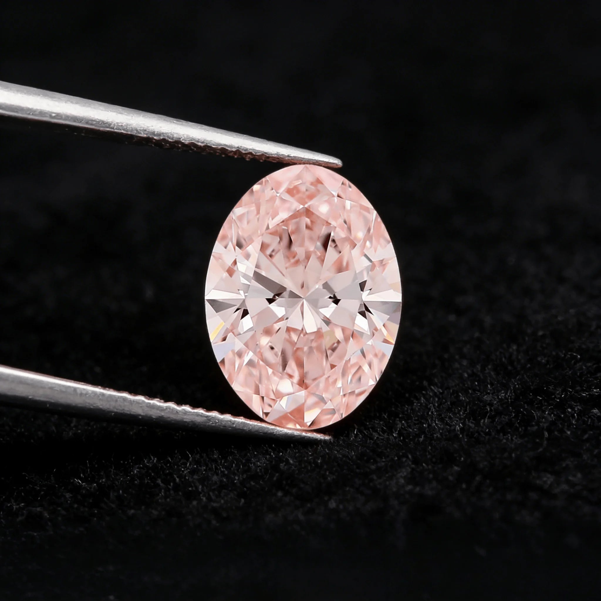 Oval fancy pink lab-grown diamond held in metal tweezers, visible facet pattern