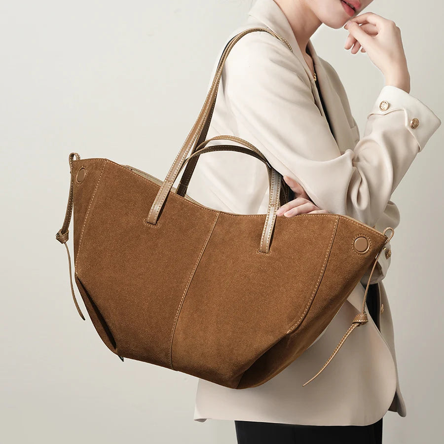 Large brown suede designer shoulder tote bag with thin straps and side tie details, styled for luxury women's fashion.
