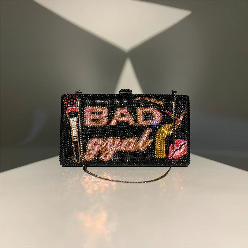Black rhinestone crystal clutch with "BAD gyal" text, makeup brush, and lip motif. Glamorous evening designer handbag.