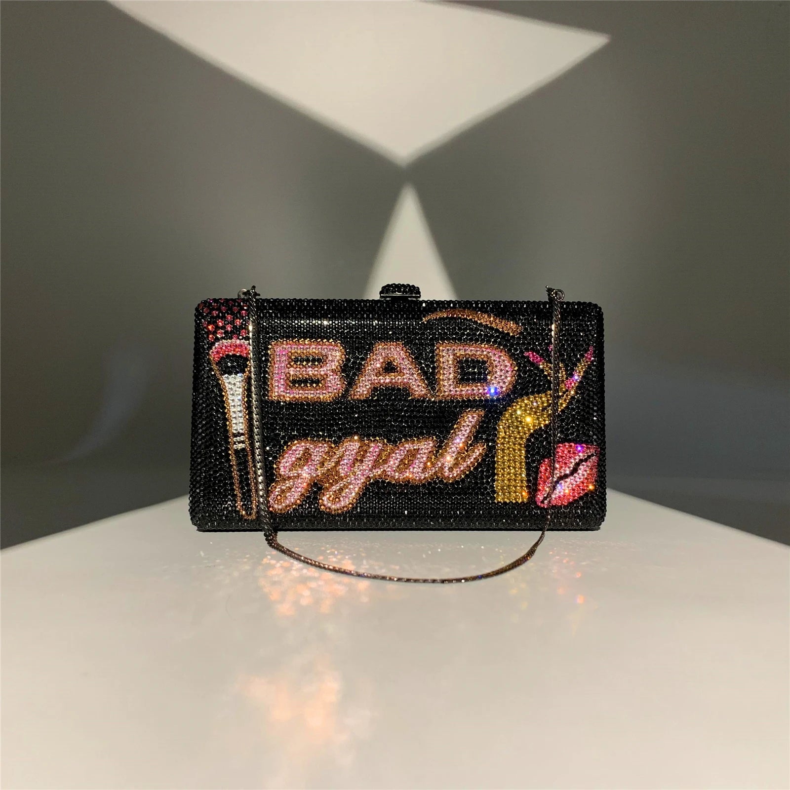 Black rhinestone crystal clutch with "BAD gyal" text, makeup brush, and lip motif. Glamorous evening designer handbag.
