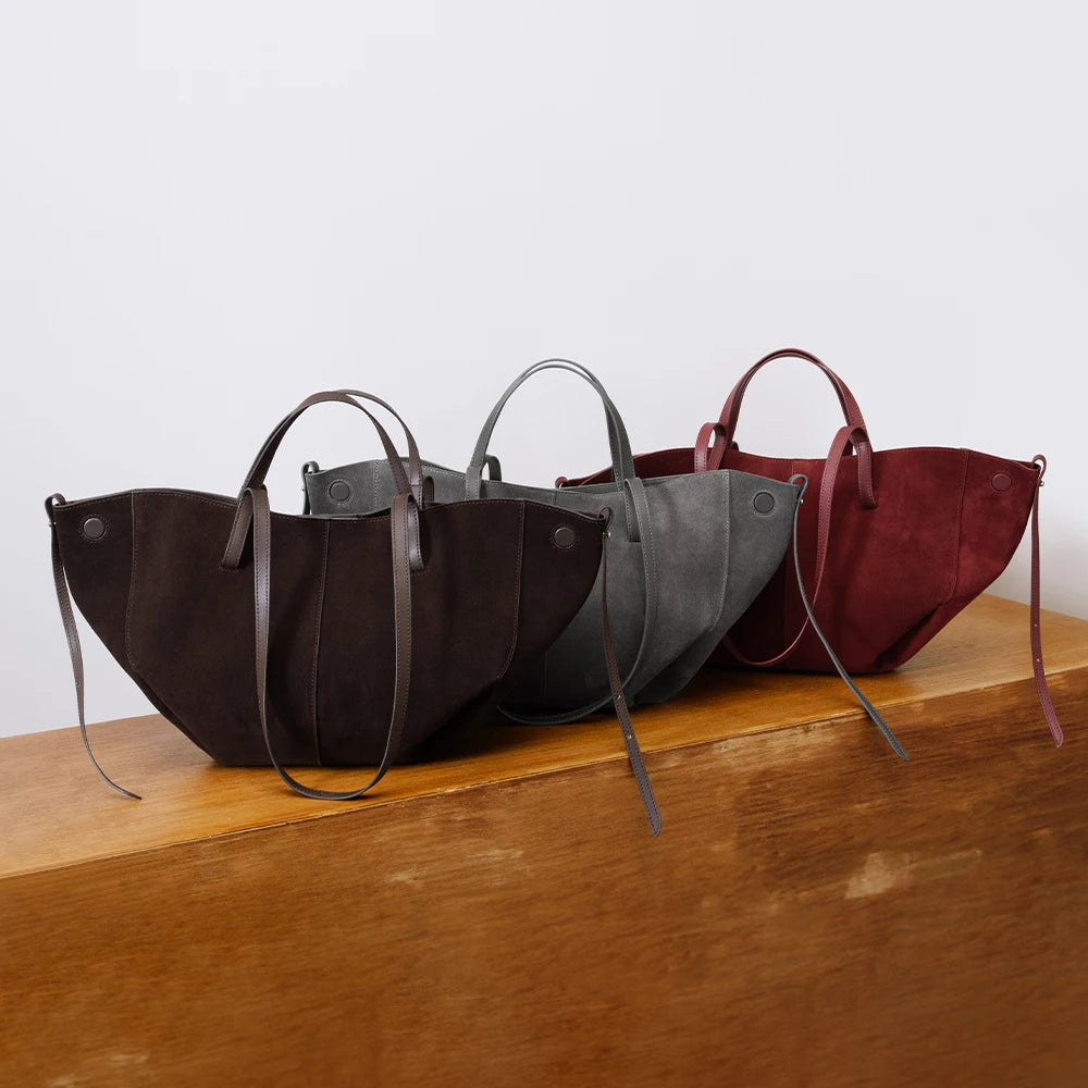 Three vintage designer suede leather handbags in brown, grey, and burgundy with structured handles on a wooden table.