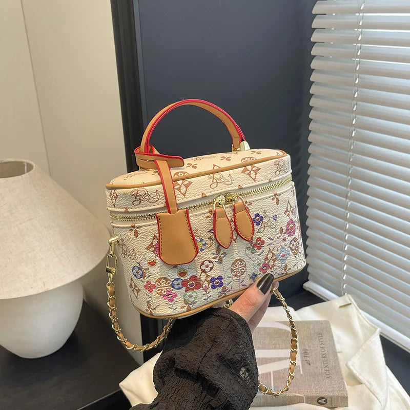 Cream genuine leather vanity trunk bag with multi-color flower monogram, red trim, top handle, and gold chain strap.