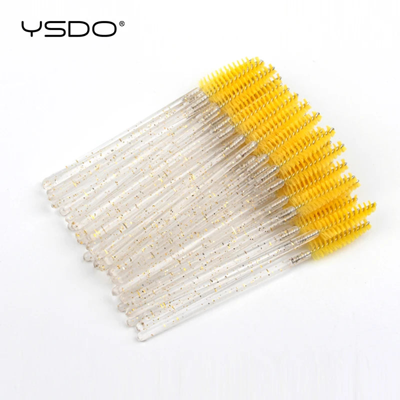 Disposable spoolie brushes with yellow bristles and clear, gold-flecked handles for eyelash and eyebrow grooming.