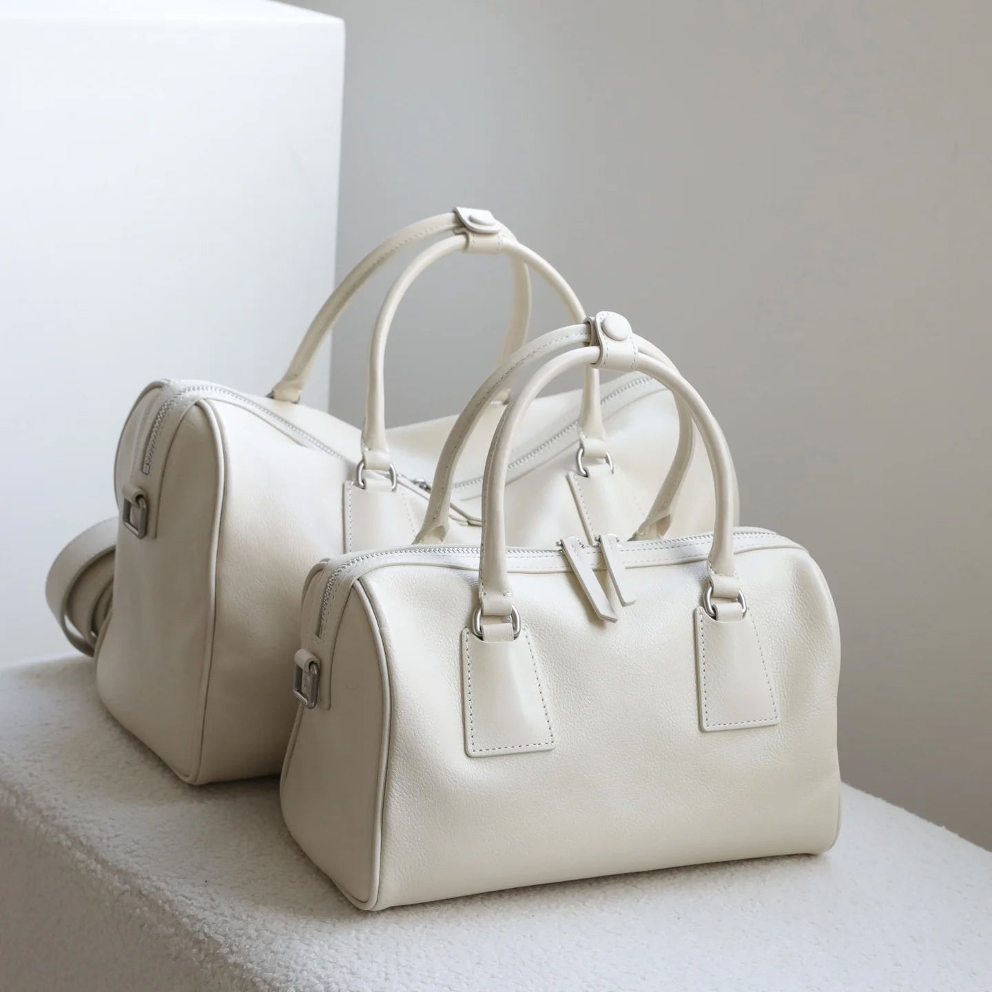Off-white vegetable-tanned leather minimalist Boston bags with dual zip closures and large-capacity top handles.