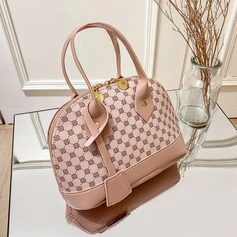 Pink designer shell handbag with monogram pattern, gold zipper hardware, and top handles for daily fashion.