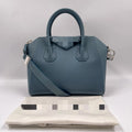 Blue genuine leather designer tote bag with top handles, crossbody strap, and classic structural trapezoid shape.