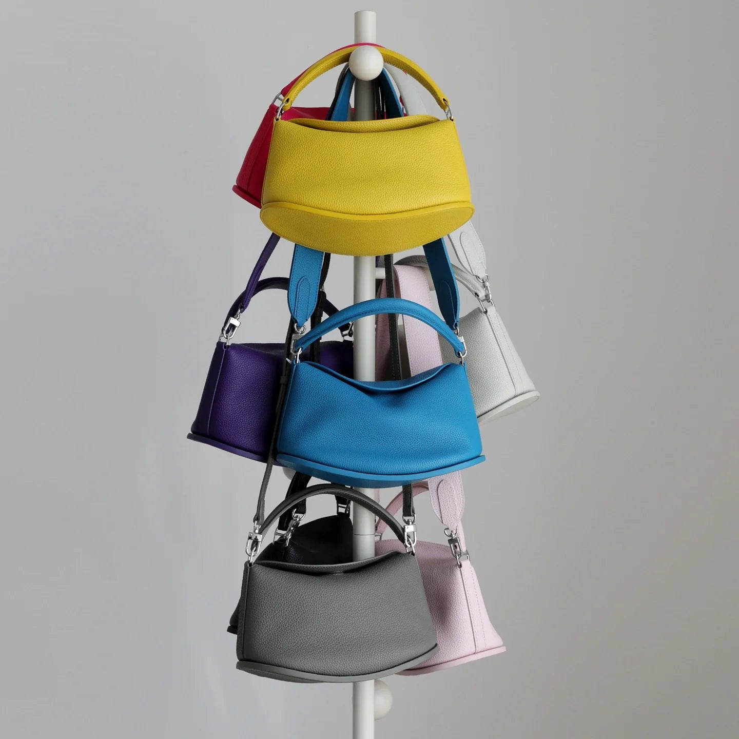 Colorful leather pillow handbags hanging on a rack. Designer cowhide commuting purses with dual straps and magnetic closure.