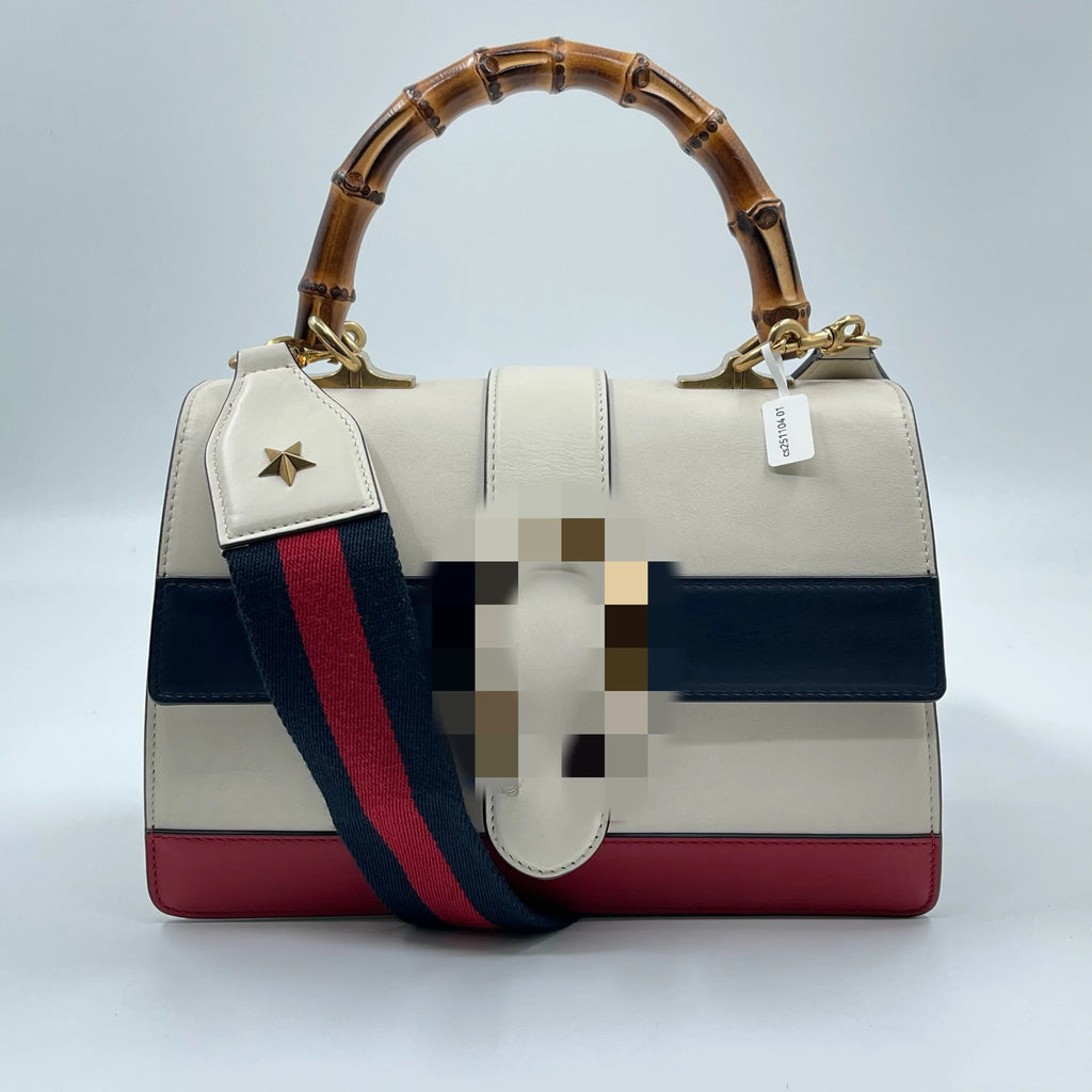 Luxury white leather designer handbag with bamboo handle, blue and red striped webbing strap, and gold star detail.