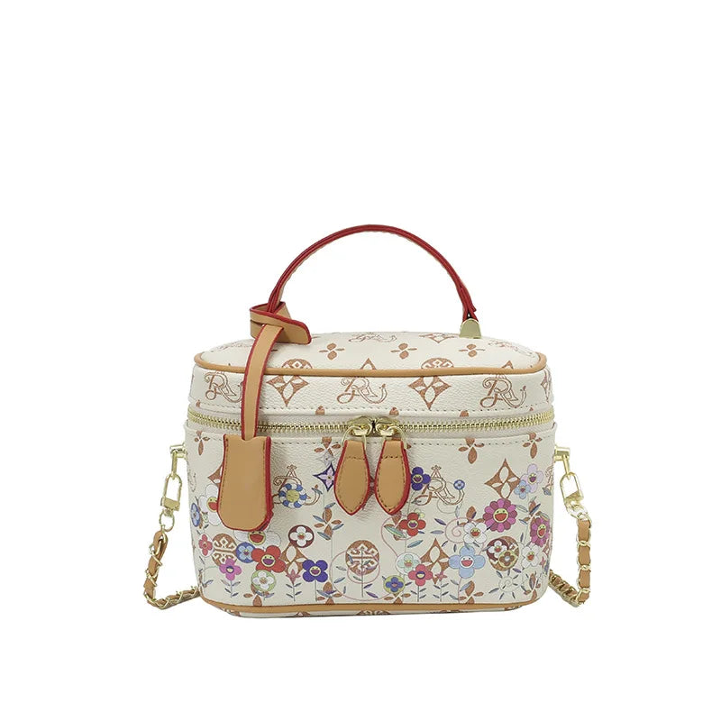 Cream genuine leather trunk bag with floral print, red handle, gold hardware, and detachable chain crossbody strap.