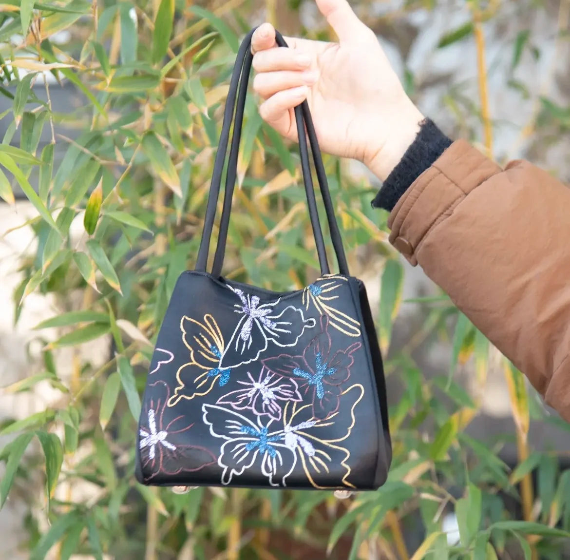 Black designer handbag with colorful floral Su embroidery, featuring slim handles for daily wear.