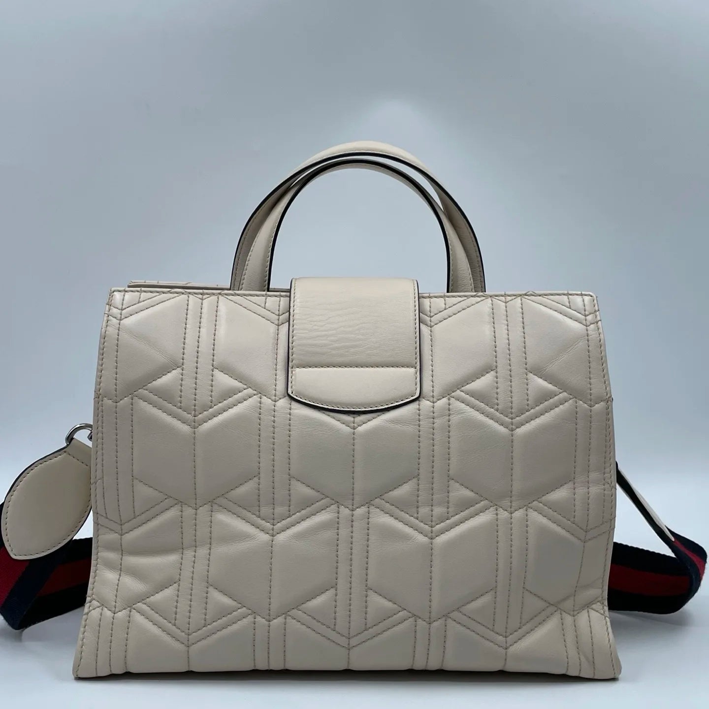 Off-white quilted leather designer tote bag with geometric stitching, top handles, and red-blue striped shoulder strap.