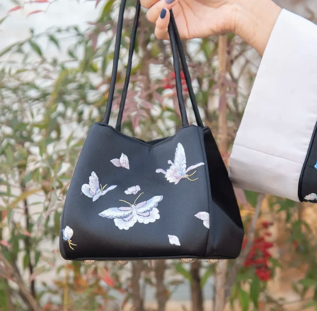 Black satin handbag with delicate white butterfly Su embroidery and twin shoulder straps for daily fashion.