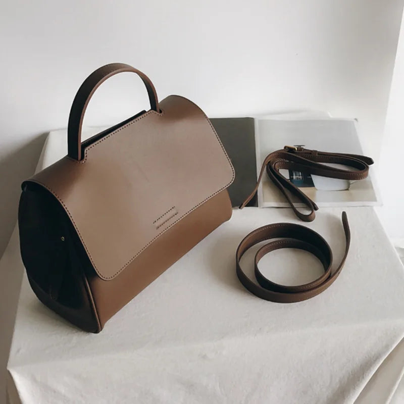 Minimalist brown leather designer handbag with top handle, flap closure, and detachable crossbody strap. Korean style.