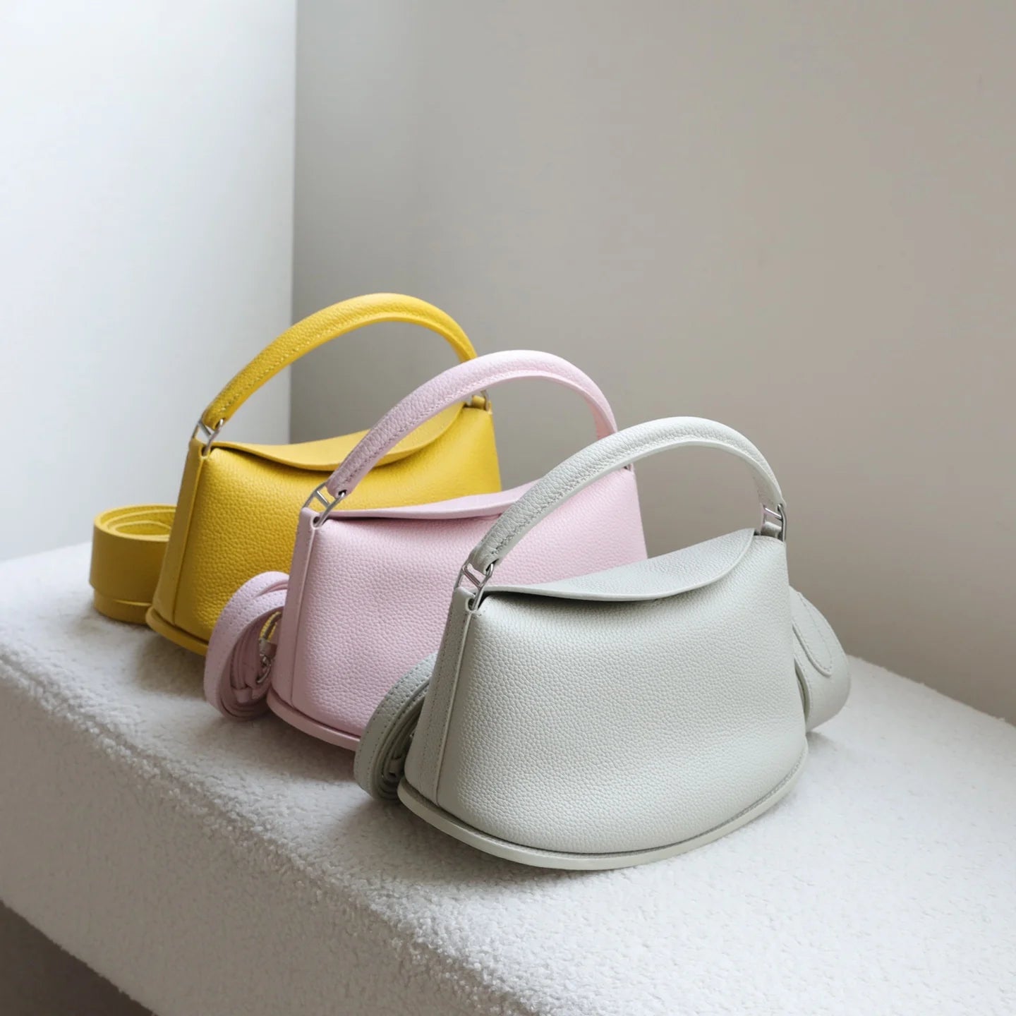 Yellow, pink, and grey pebble-grain cowhide designer handbags with two straps and a casual pillow-shaped silhouette.