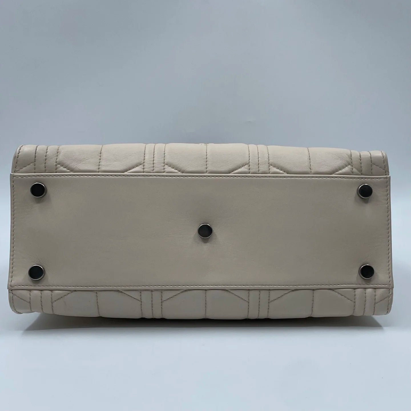 White designer handbag bottom view, quilted leather shoulder tote with protective metal feet. Luxury second-hand style.