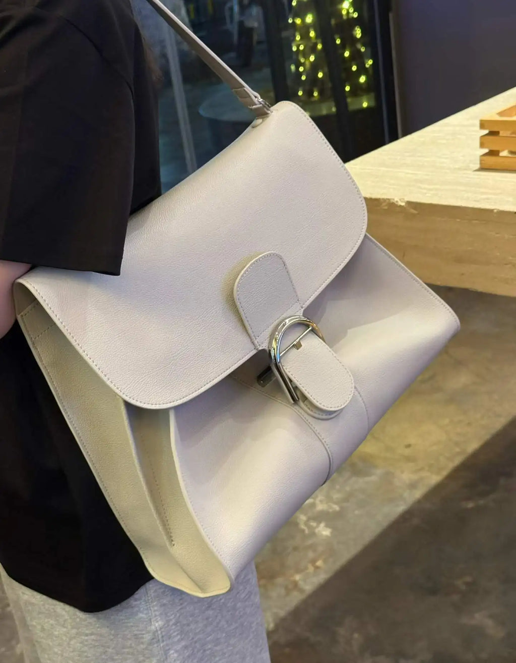 Off-white leather shoulder bag with structured flap, silver buckle closure, and elegant designer tote silhouette.