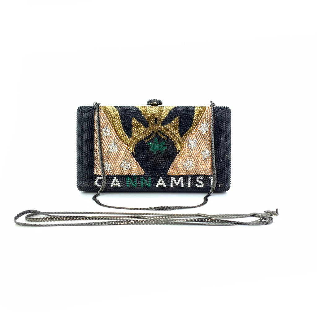 Black crystal-encrusted designer clutch bag with gold and green beaded artwork, chain strap, and "CANNAMIST" lettering.