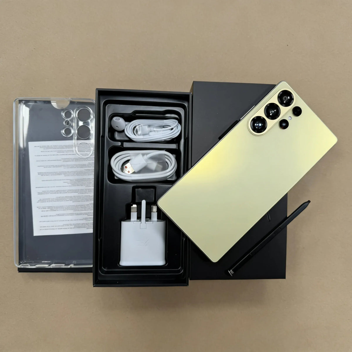 Gold smartphone with quad rear cameras and open box accessories, earbuds, cables, charger