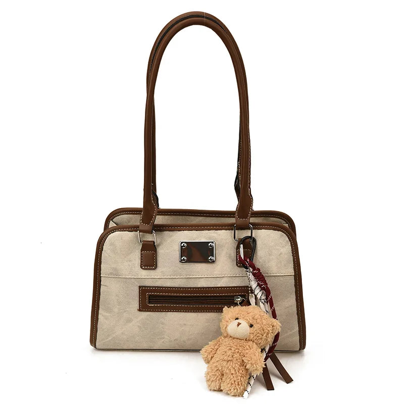 Beige suede and brown leather trunk-style tote bag with a zipper pocket and a cute teddy bear charm.