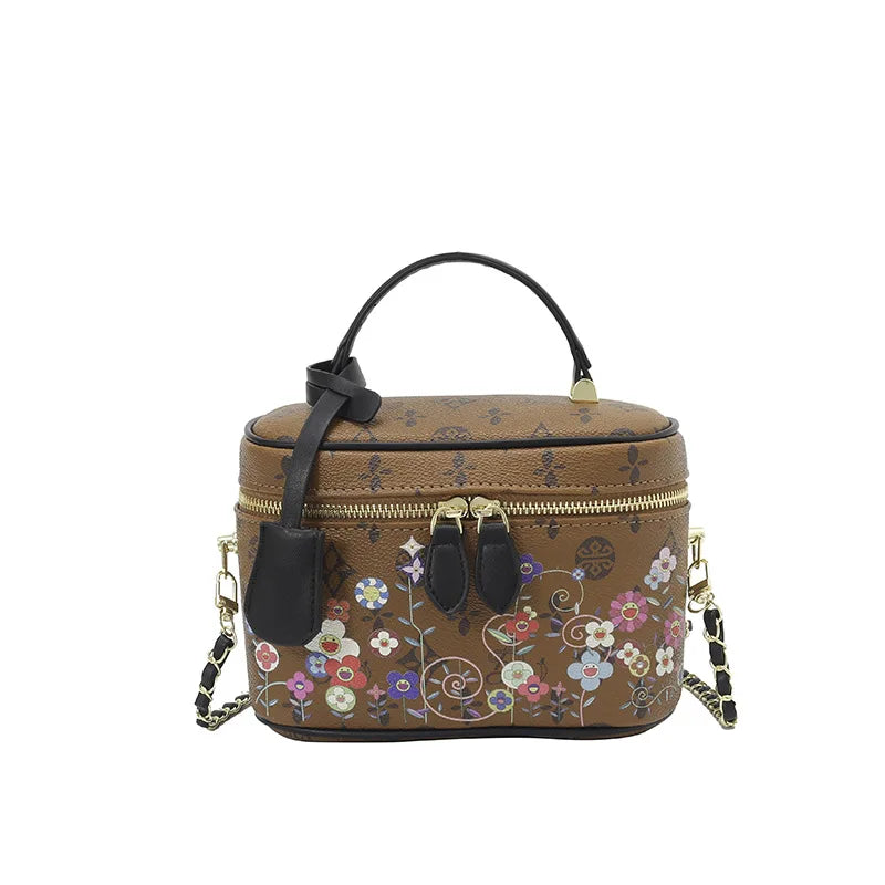 Brown genuine leather trunk crossbody bag with floral pattern, black top handle, and gold chain shoulder strap.