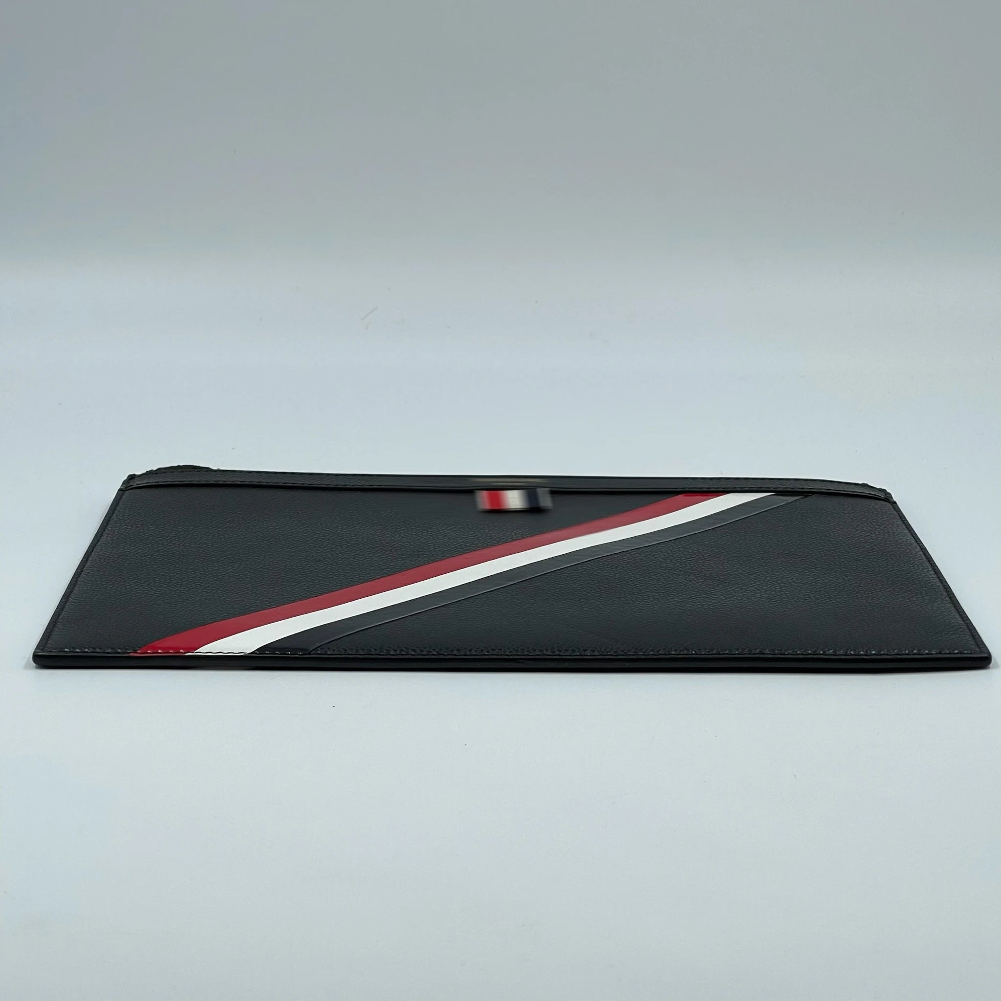 Black leather designer clutch featuring a diagonal red, white, and blue stripe detail for a travel-ready aesthetic.