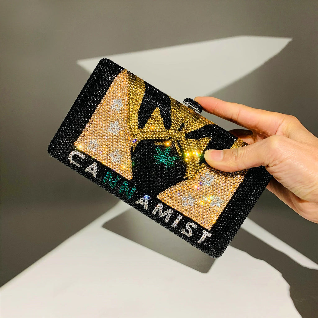 Black, gold, and green crystal-encrusted designer clutch bag with leaf motif and "CANNAMIST" text for evening wear.