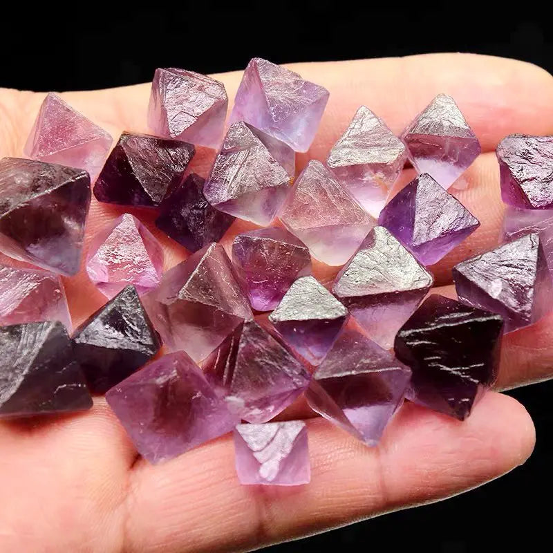 Purple rough crystal octahedra pieces spread in palm, sharp faceted surfaces