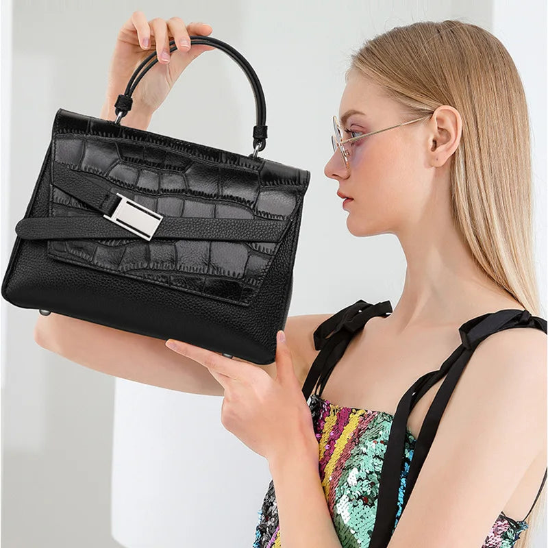 Black genuine leather designer handbag with crocodile-embossed flap, top handle, and silver buckle detail.