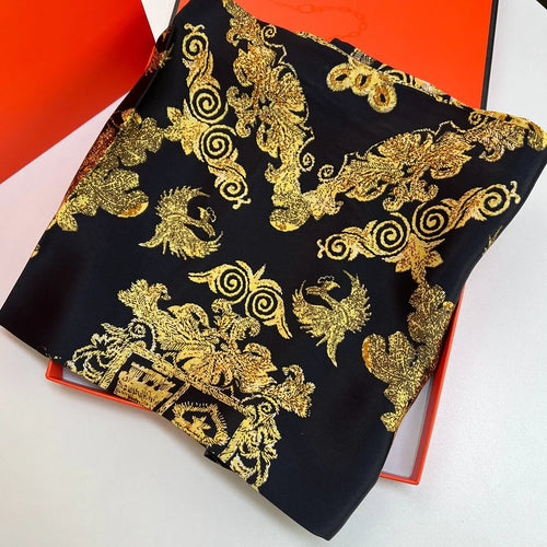 Luxury square silk scarf in black and gold featuring ornate baroque patterns and phoenix motifs in a designer gift box.