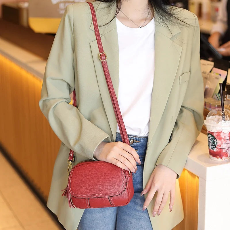 Red genuine leather designer crossbody bag with tassel detail and adjustable shoulder strap, styled as a mini handbag.