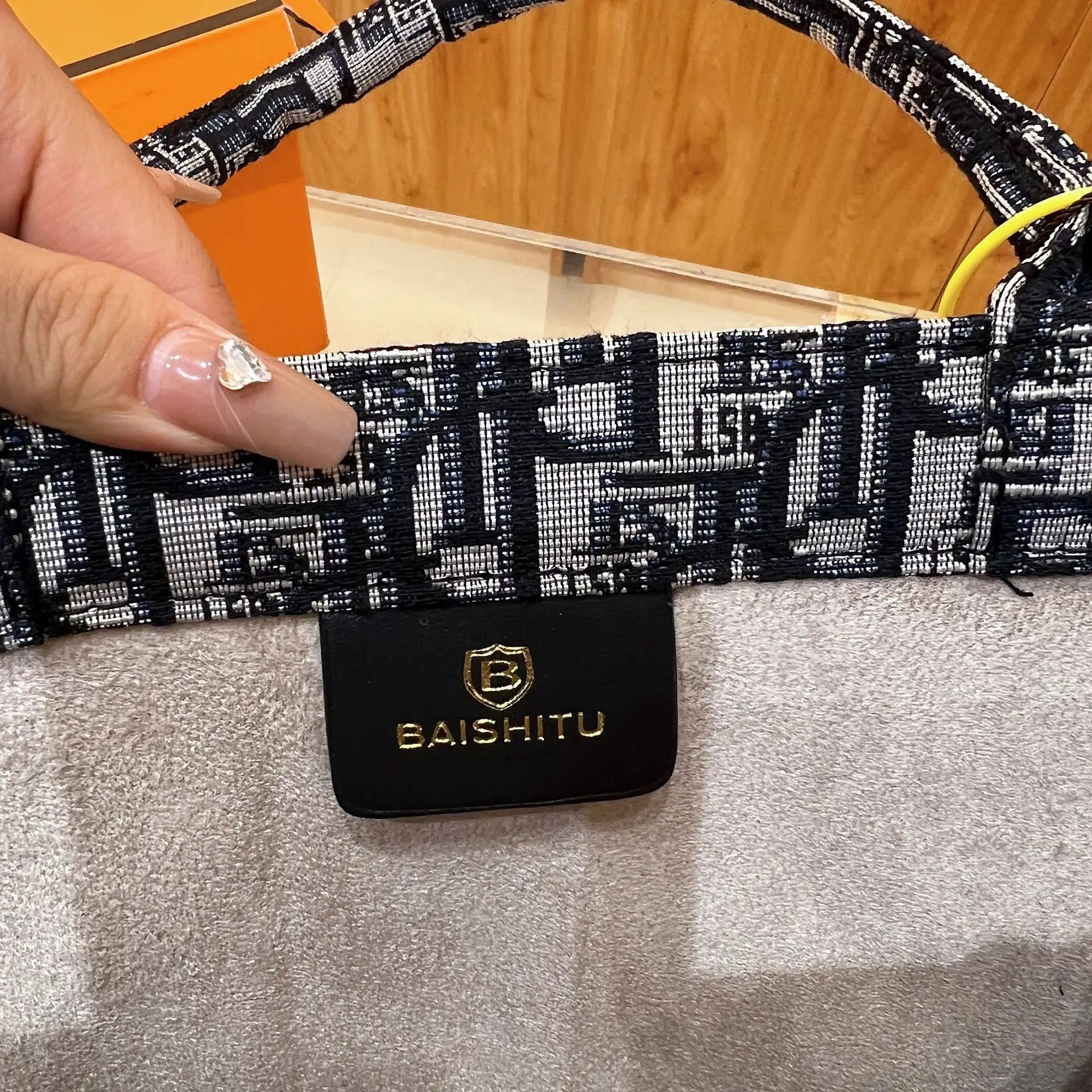 Beige cowhide handbag with Baishitu gold logo patch and black-and-white patterned embroidered fabric shoulder strap.